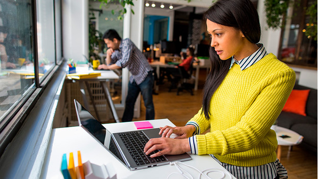 Woman in yellow sweater works on a laptop.