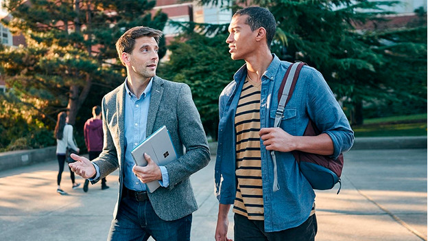 Man walks outside with Surface Pro under his arm and talks to another man.