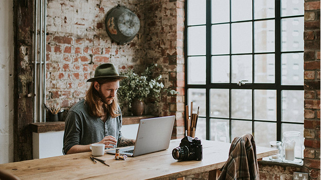 Hipster with long hair and hat works behind Acer Chromebook. Camera is on the table.