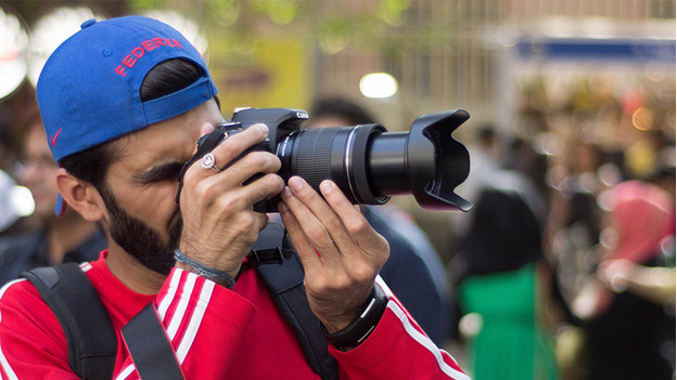 Man with red sweater and blue cap takes photo with camera.