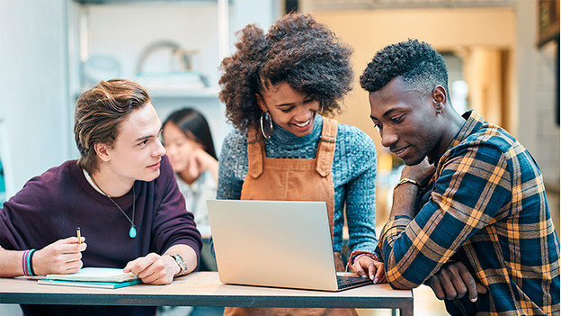 Three students work together behind the laptop.