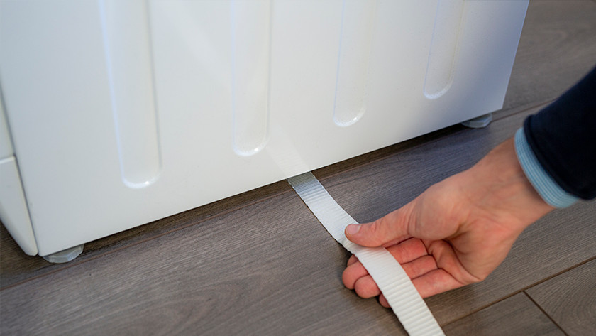 Führe den Gurt genau mittig unter der Waschmaschine hindurch.