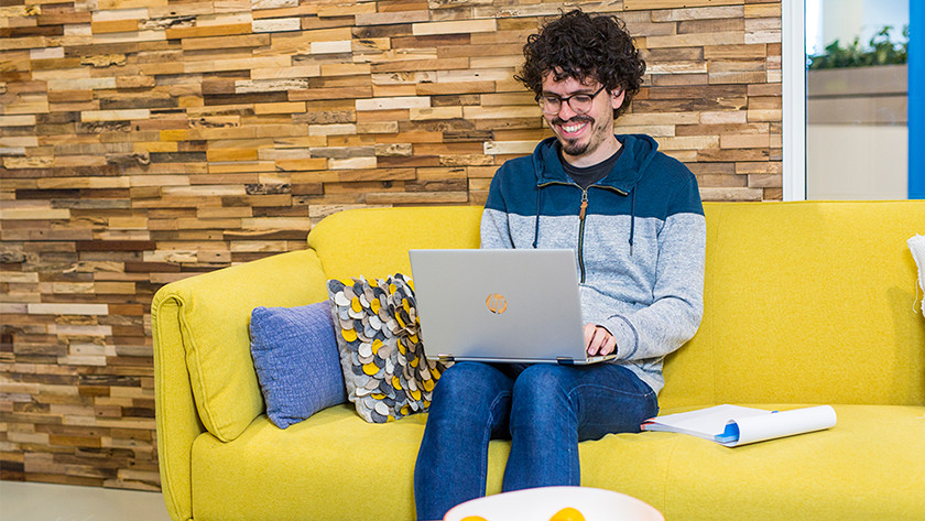 Person on yellow couch works on HP laptop.