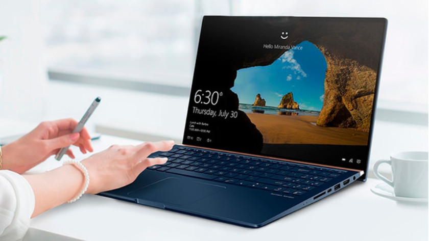 Woman works on 15-inch laptop with coffee cup next to her.