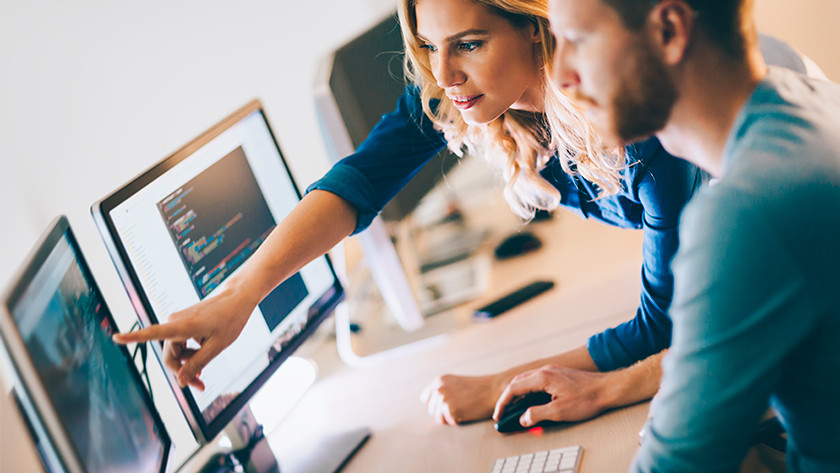 Frau zeigt auf den Monitor des Computers auf dem Schreibtisch. Mann schaut mit Computermaus in der Hand zu.