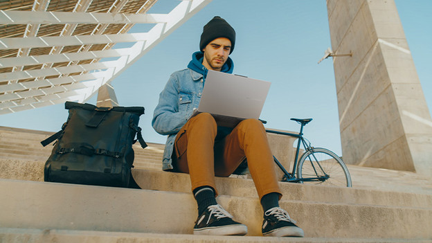 Mädchen tippt auf einem Laptop. Ein Handy liegt auf dem Tisch.