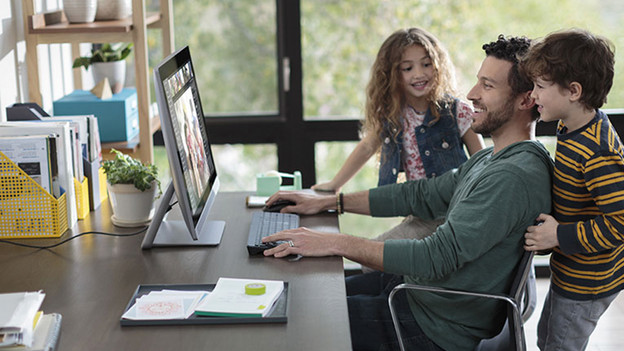 Man with two children sitting at desk working behind his all-in-one computer.