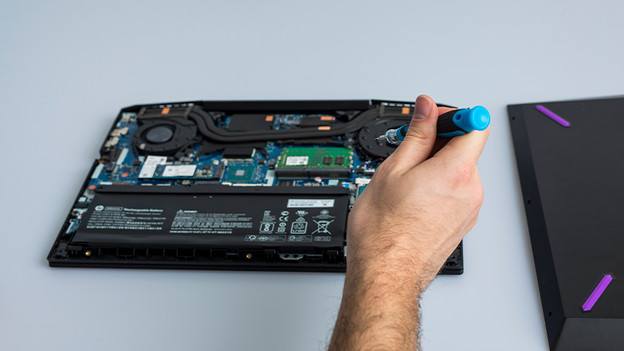 Man moves the screwdriver toward the laptop.