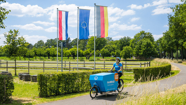 Coolblue worker on a bicycle in front of 3 flags